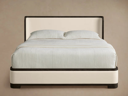 Darien Curved Shelter Bed, cream upholstered with dark frame, curved headboard & light ribbed bedding on a wood floor.