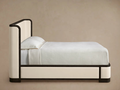 Close-up of Darien Curved Shelter Bed's dark wooden frame with visible grain, curving around a light cream upholstered panel.