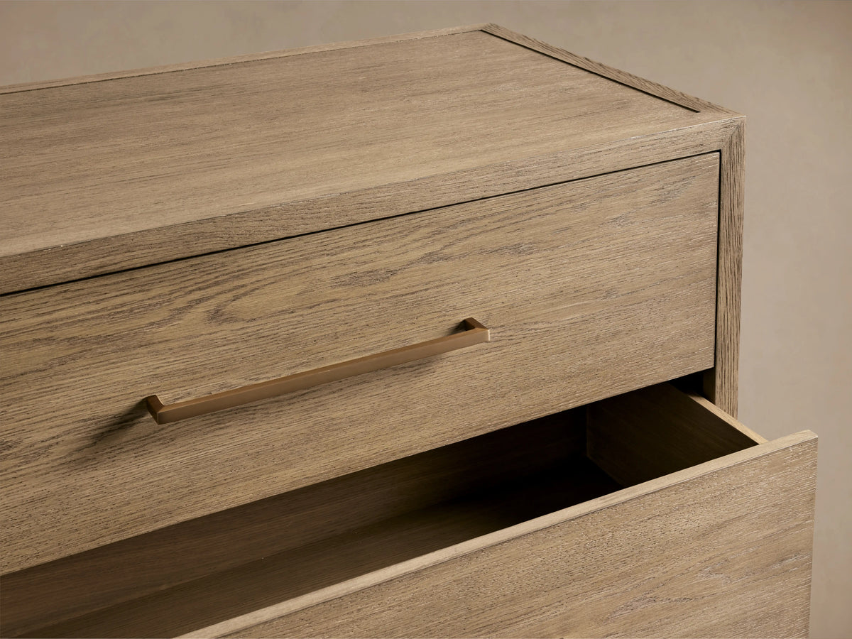 Darwyn Five-Drawer Dresser in oak wood, close-up of top drawer with brass pull, partially open below.