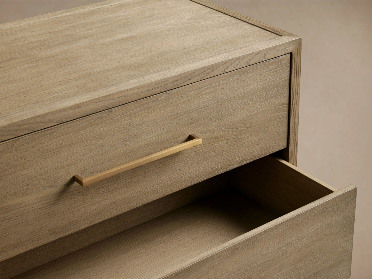 Darwyn Six-Drawer Dresser made of oak with oak veneers, featuring brass drawer pulls and a hand-applied finish, against a beige wall.