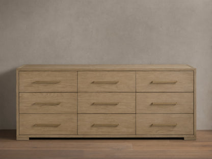 Front view of the light natural oak Darien Nine-Drawer Dresser with nine drawers and long brass-colored handles.