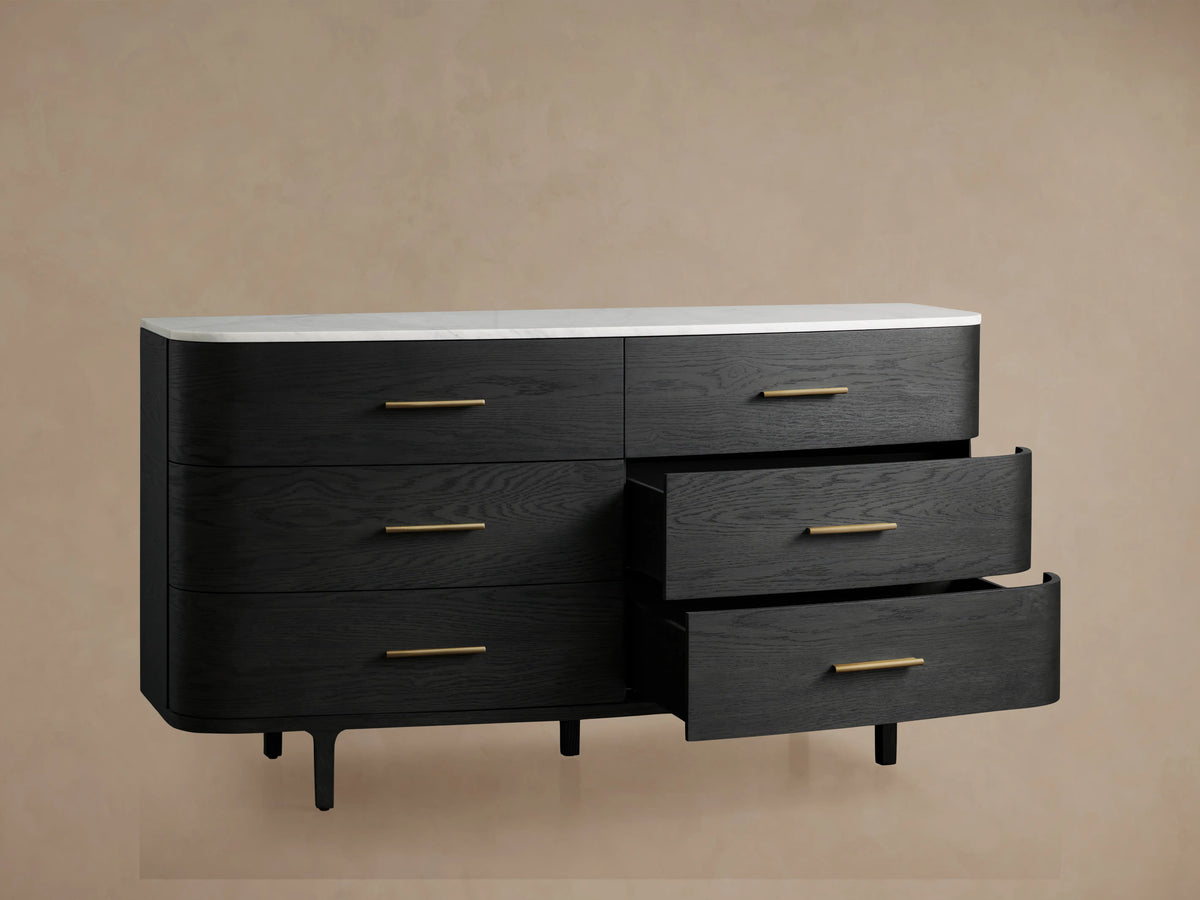 Danny Six-Drawer Dresser in ebony finish with brass pulls and a white marble top on a wooden floor, curved front.