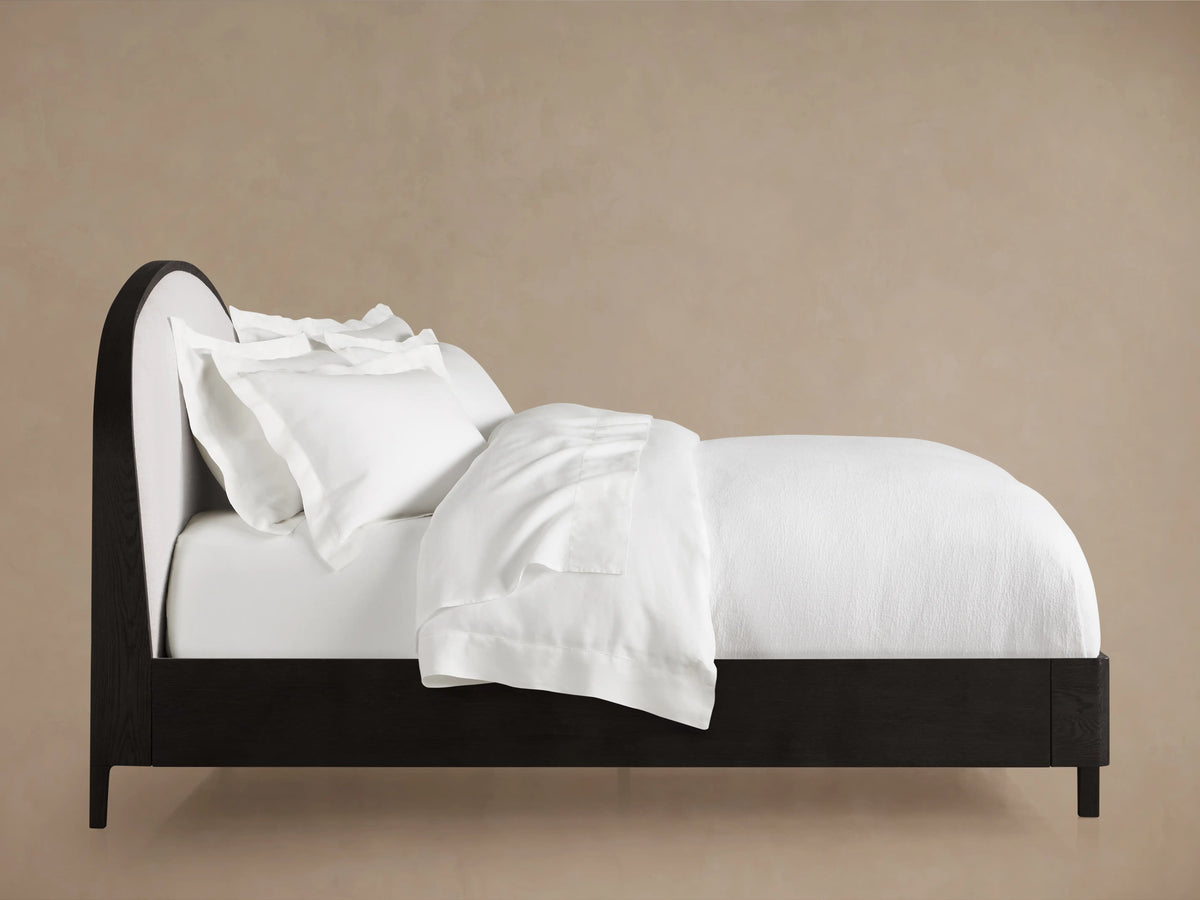 Danny Bed with ebony oak frame, curved upholstered white headboard, and white bedding against a neutral background.