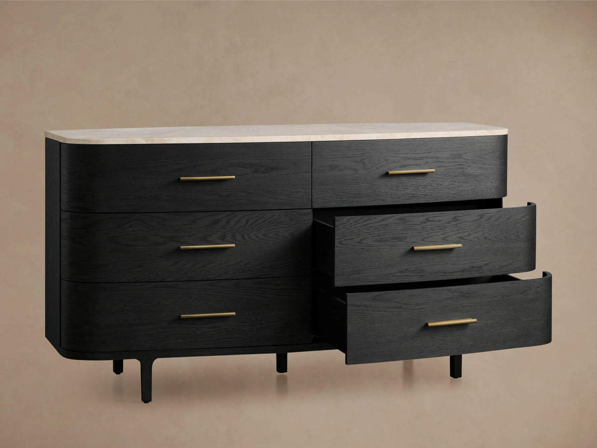 Danny Six-Drawer Dresser in ebony finish, features smooth, curved design with brass pulls and white marble top on wooden floor.