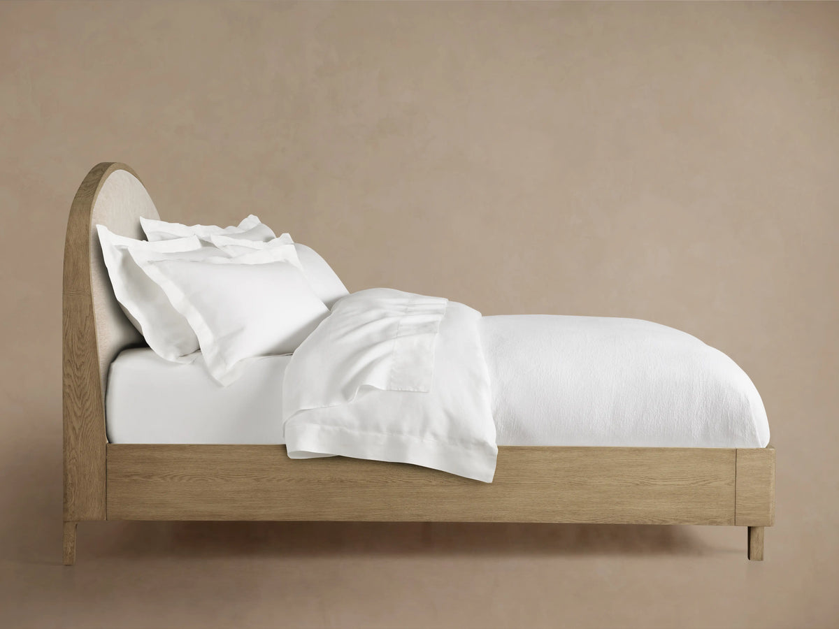 Rounded corner of Danny Bed's headboard, crafted from oak wood with beige fabric upholstery and visible wood grain texture.