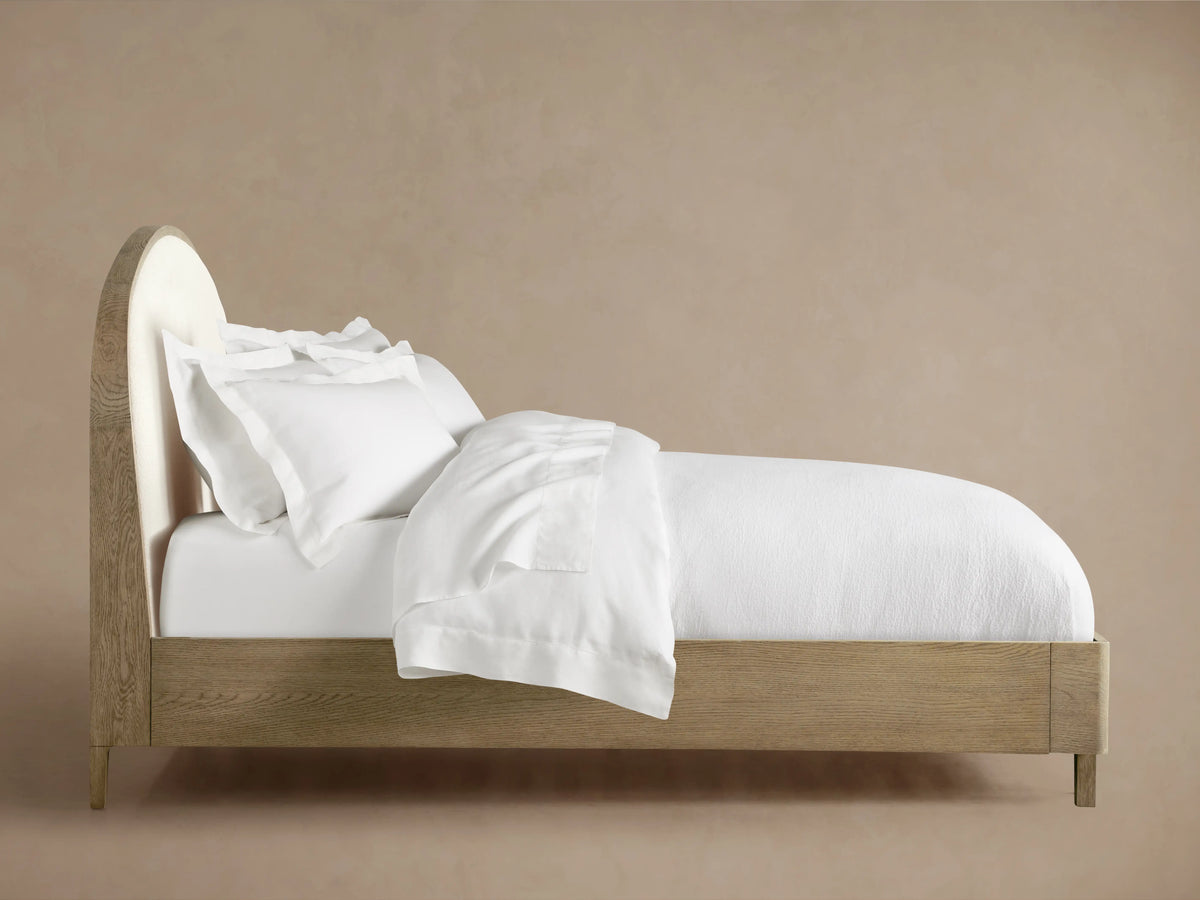 Danny Bed with oak wood frame in fawn finish, featuring upholstered headboard. Dressed in white bedding, side view.