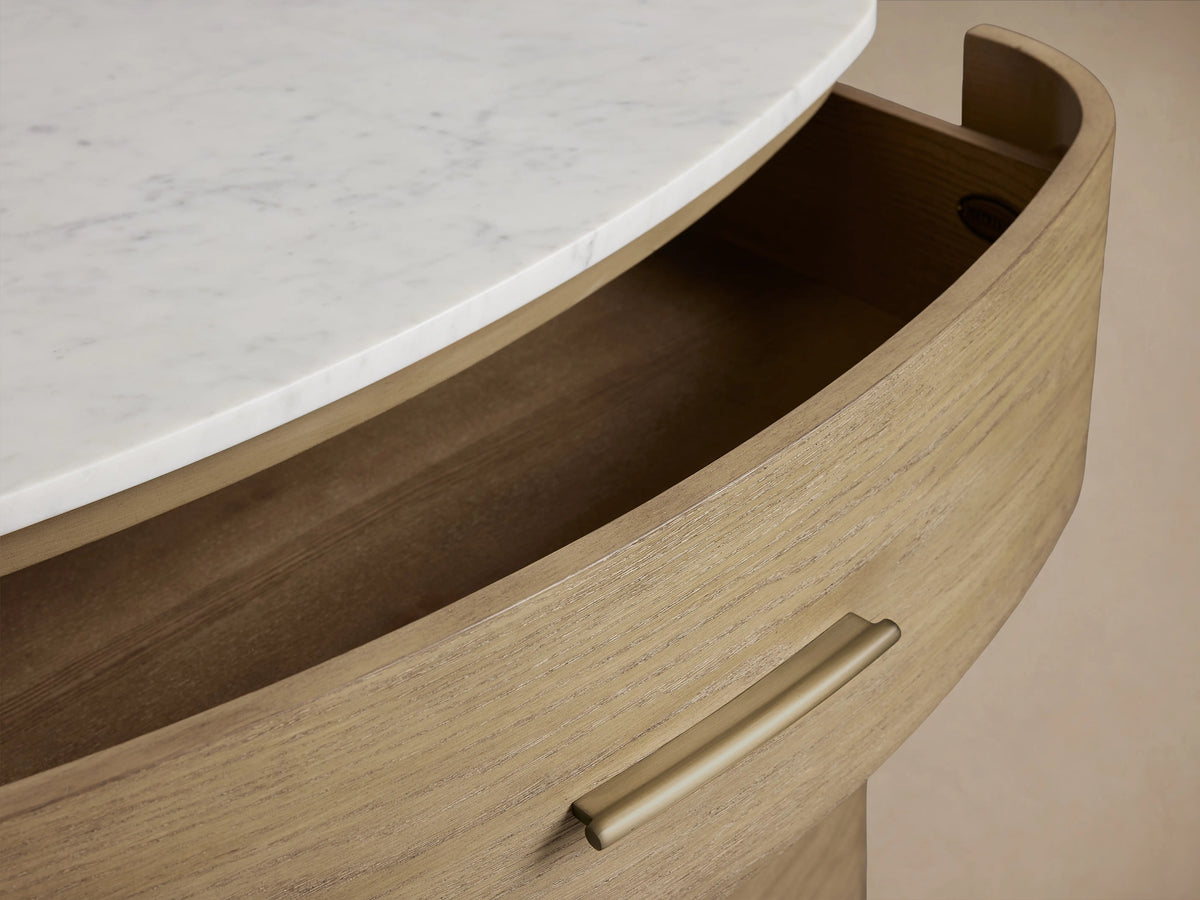 Curved oak dresser with an open drawer, featuring a brass pull and a cream marble top with visible swirls.
