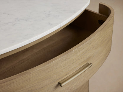 Curved oak dresser with an open drawer, featuring a brass pull and a cream marble top with visible swirls.