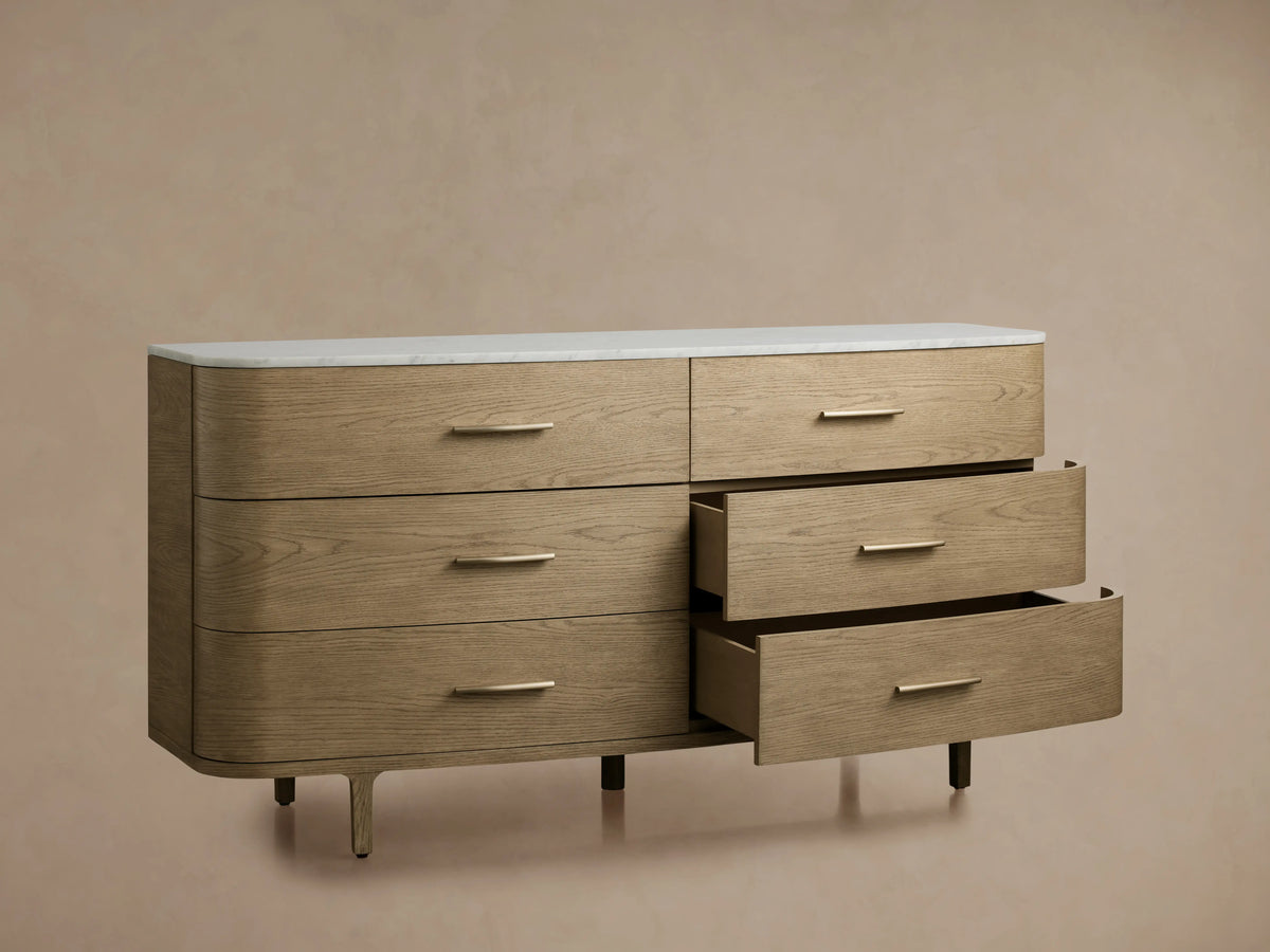 Danny Six-Drawer Dresser in oak with a cream marble top, three open drawers showing brass pulls, on a beige background.