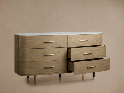 Danny Six-Drawer Dresser in oak with a cream marble top, three open drawers showing brass pulls, on a beige background.