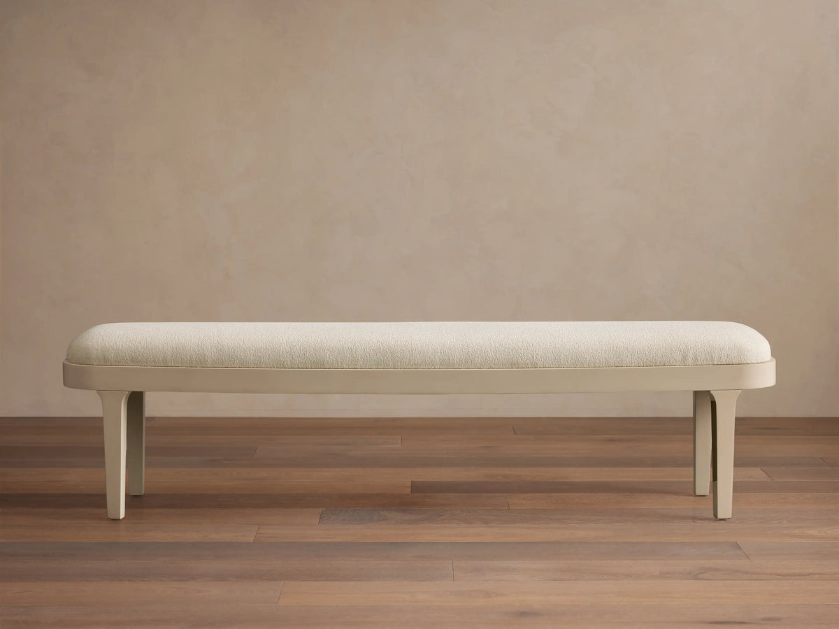 Danny Bench in Fumo. Off-white upholstered top with rounded edges and a sleek matching frame, seen frontally on a wood floor.