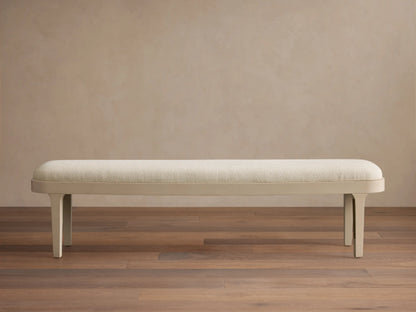 Danny Bench in Fumo. Off-white upholstered top with rounded edges and a sleek matching frame, seen frontally on a wood floor.