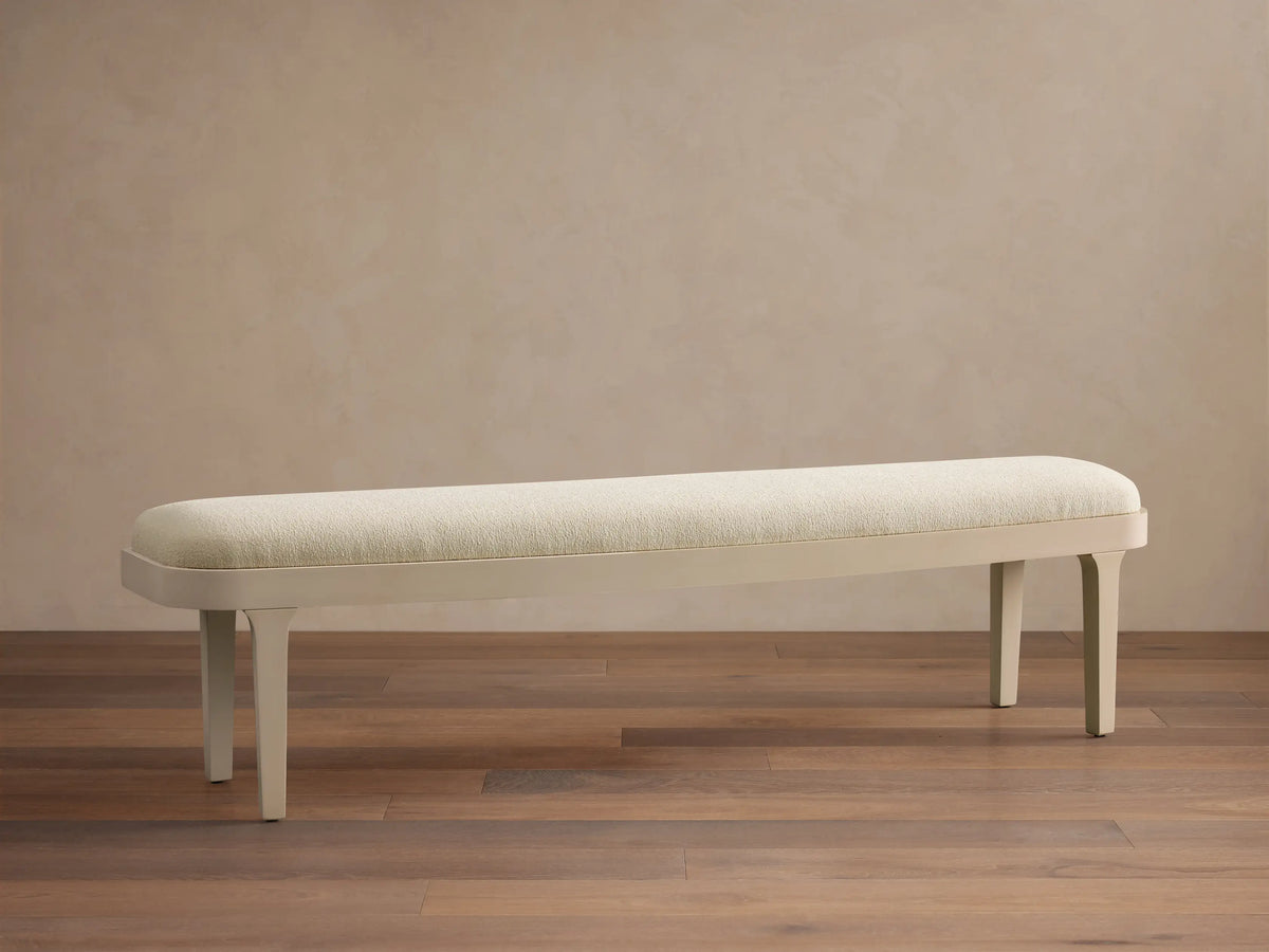 Danny Bench in Fumo. Off-white upholstered top with rounded edges and a sleek matching frame, seen frontally on a wood floor.