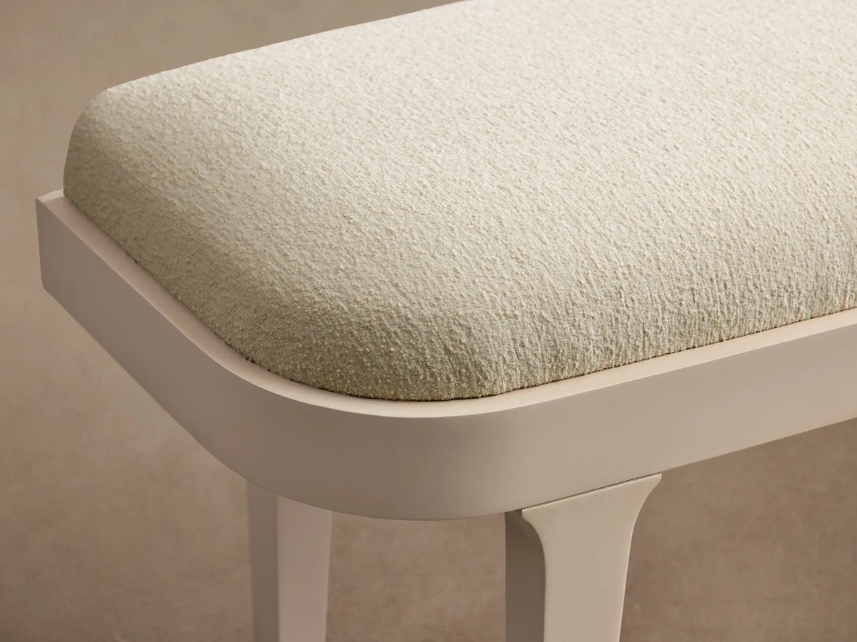 Danny Bench in Fumo: long, upholstered bench with light cream fabric top, light greige frame & straight legs on a wood floor.