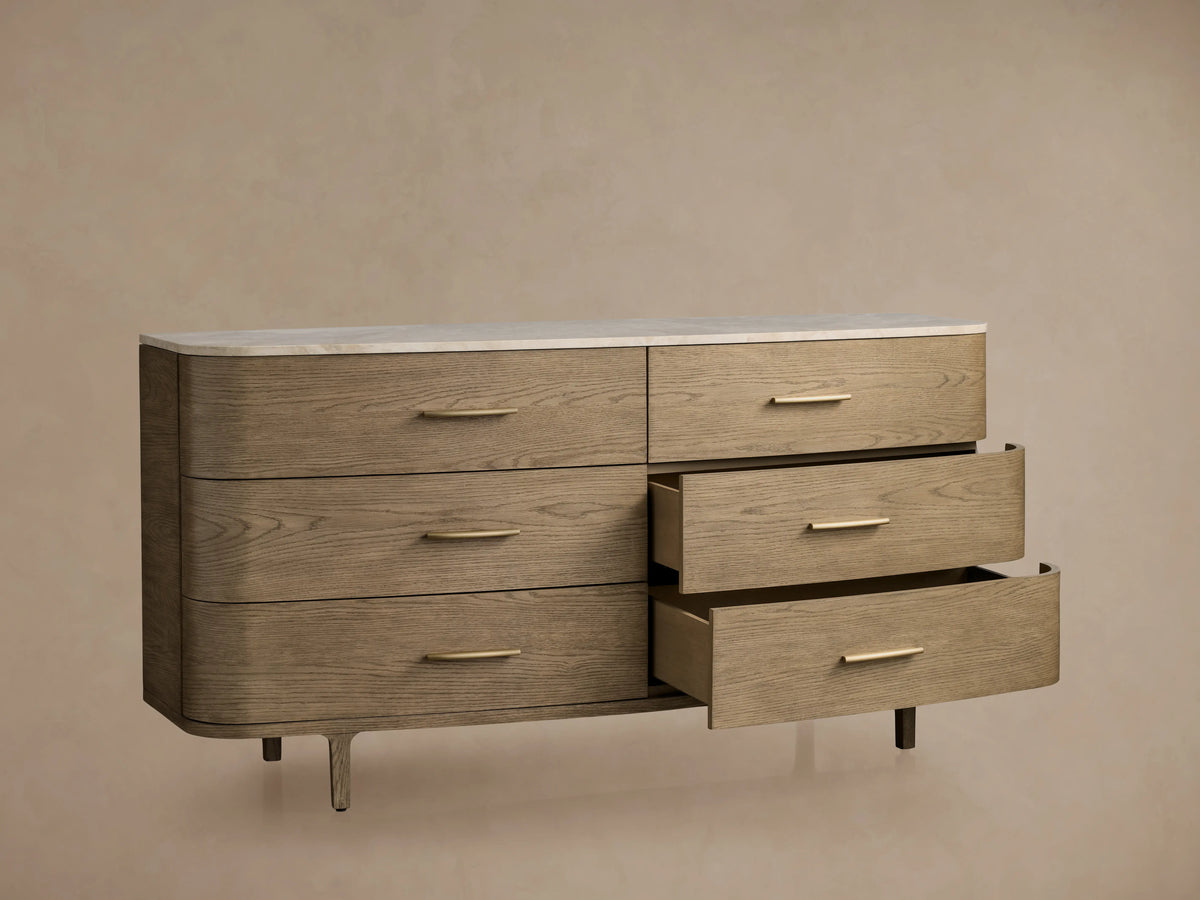 Danny Six-Drawer Dresser in oak with fawn finish, featuring a white marble top and brass pulls. Some drawers open, showcasing design.