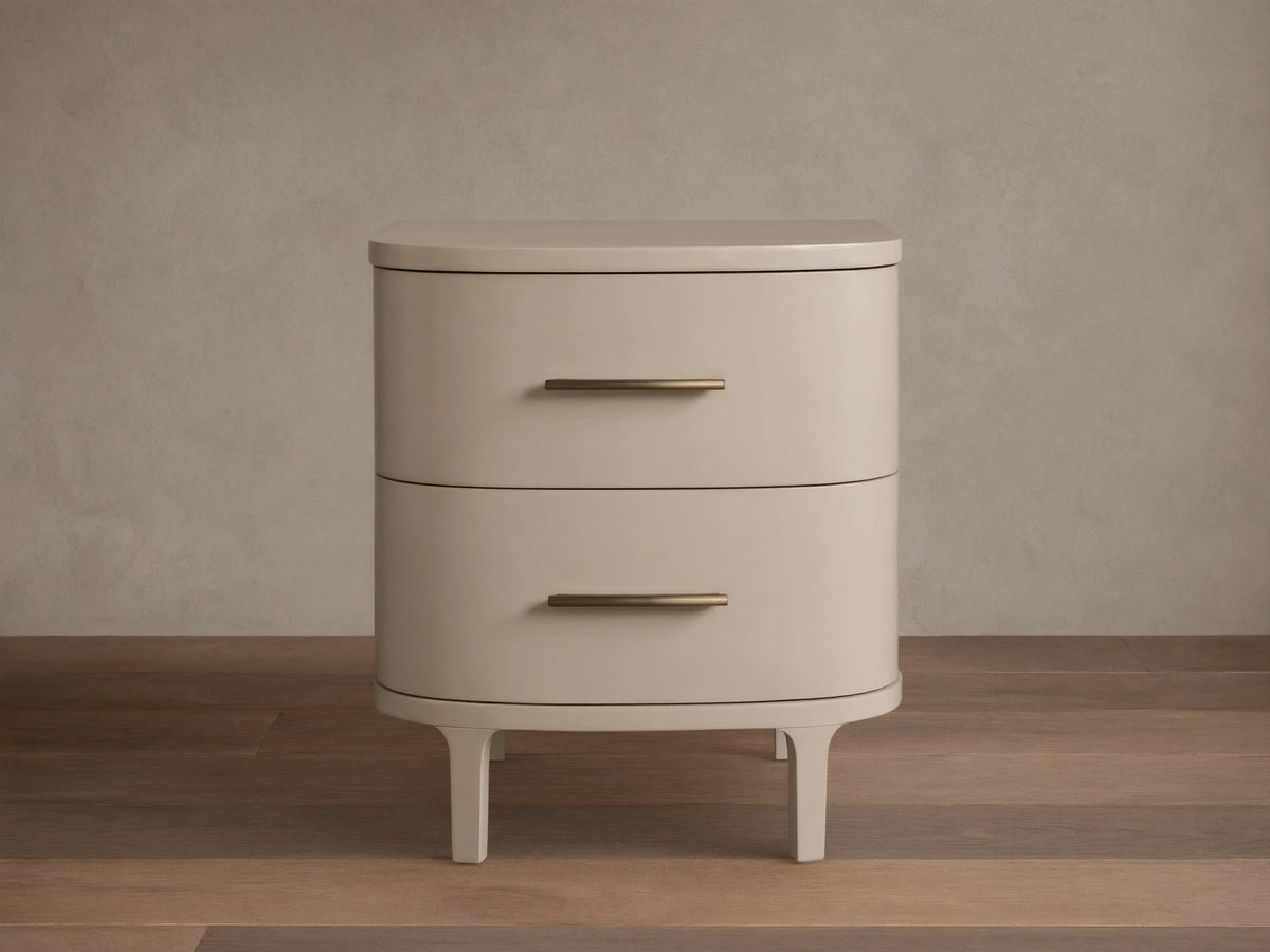 Danny Nightstand in fumo: light beige, rounded nightstand with two drawers, horizontal brass pulls, on short splayed legs.