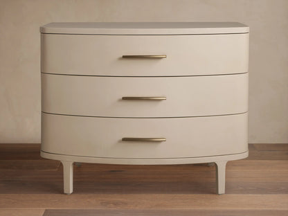 Danny Three-Drawer Chest in Fumo. Light grayish-beige finish, rounded front, 3 drawers with brass pulls, on wood floor.
