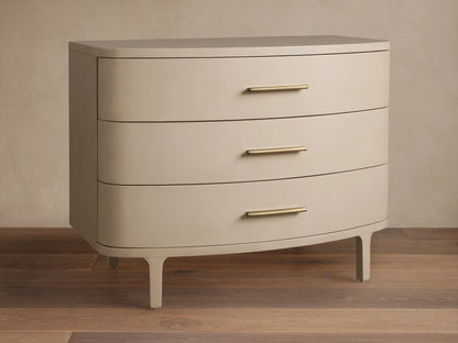 Danny Three-Drawer Chest in Fumo. Light grayish-beige finish, rounded front, 3 drawers with brass pulls, on wood floor.