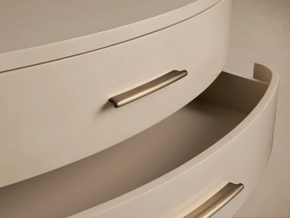 Danny Fumo Three-Drawer Chest. Light greyish-beige chest with curved fronts, 3 brass pulls, short legs, on wooden floor.