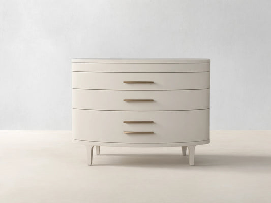 Danny Three-Drawer Chest in Fumo. Light grayish-beige finish, rounded front, 3 drawers with brass pulls, on wood floor.