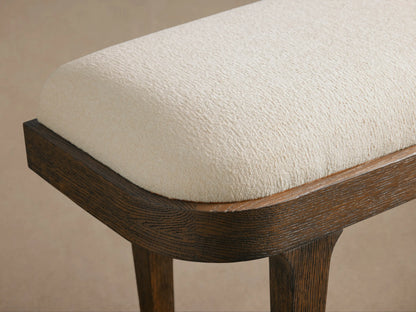 Danny Bench: Off-white upholstered seat on a dark brown oak wood frame with angled legs, on a wooden floor in a neutral room.