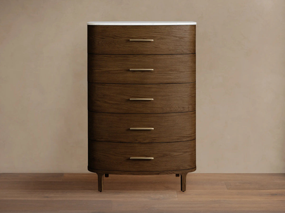 Danny Five-Drawer Dresser: Dark oak 5-drawer dresser with rounded front, brass pulls, white marble top. Standing on wooden floor.