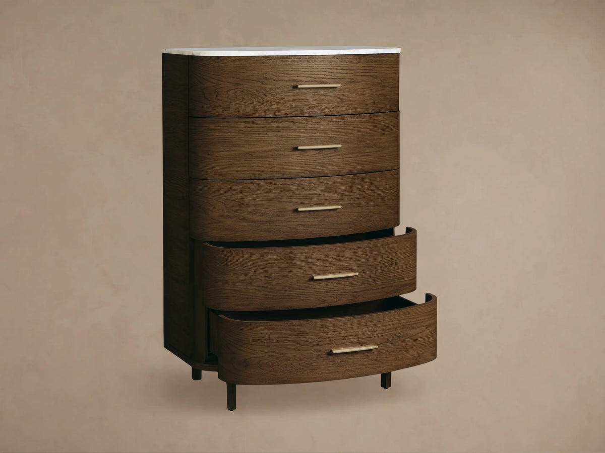 Danny Five-Drawer Dresser: Dark oak 5-drawer dresser with rounded front, brass pulls, white marble top. Standing on wooden floor.