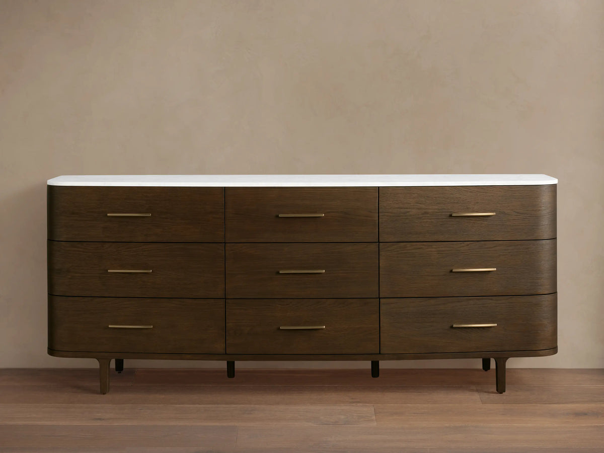 Danny Nine-Drawer Dresser: Dark oak wood with rounded edges, white marble top, nine brass-pull drawers, and tapered legs.