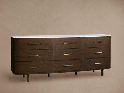 Danny Nine-Drawer Dresser: Dark oak wood with rounded edges, white marble top, nine brass-pull drawers, and tapered legs.