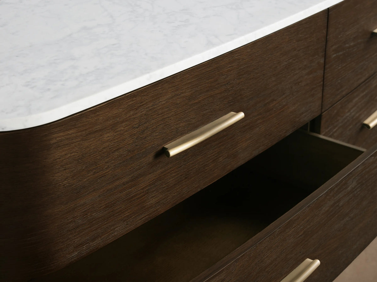 Danny Nine-Drawer Dresser; modern dark oak wood with a white marble top, nine drawers with sleek brass pulls, curved ends, on legs.