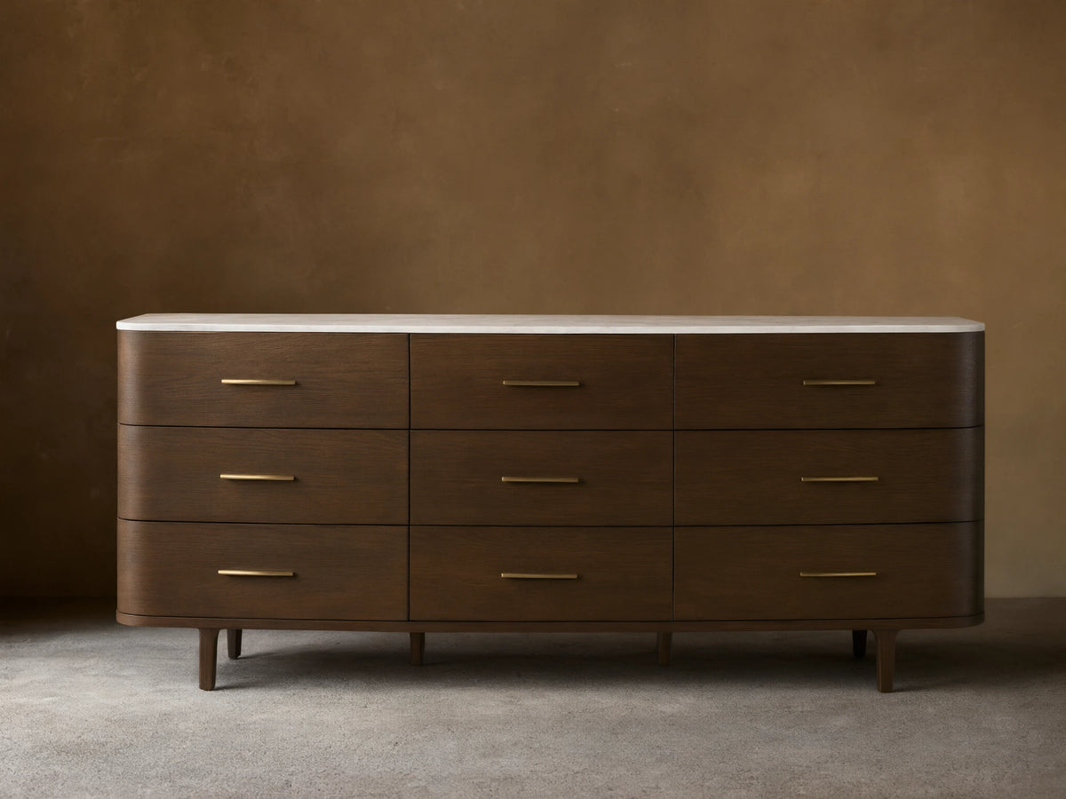 Danny Nine-Drawer Dresser: Dark oak wood with rounded edges, white marble top, nine brass-pull drawers, and tapered legs.