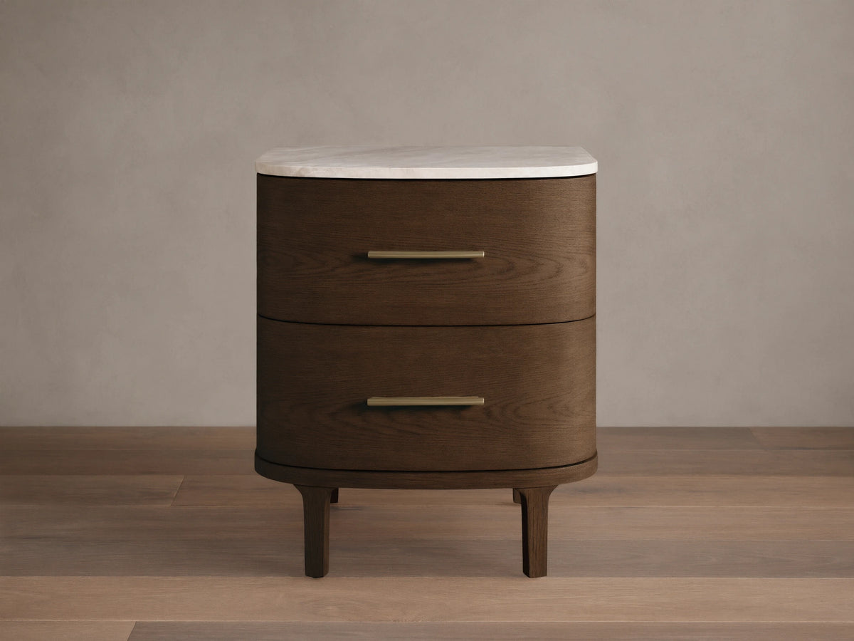 Danny Nightstand: Dark oak wood, two rounded drawers with brass pulls, white marble top, on a wood floor against a light wall.