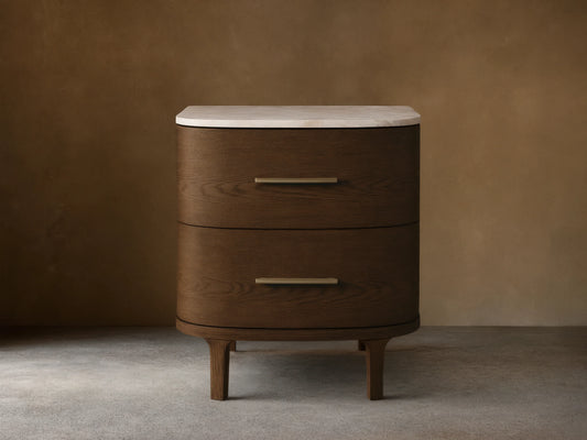 Danny Nightstand: Dark oak wood, two rounded drawers with brass pulls, white marble top, on a wood floor against a light wall.