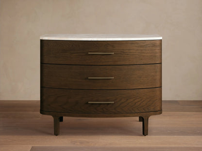 Danny Three-Drawer Chest: dark brown oak with rounded edges, white marble top, three horizontal brass handles, on wood floor.