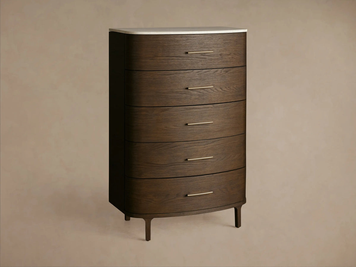 Close-up of Danny Five-Drawer Dresser. Dark oak wood with curved fronts, cream marble top, and brass pull. Top drawer ajar.