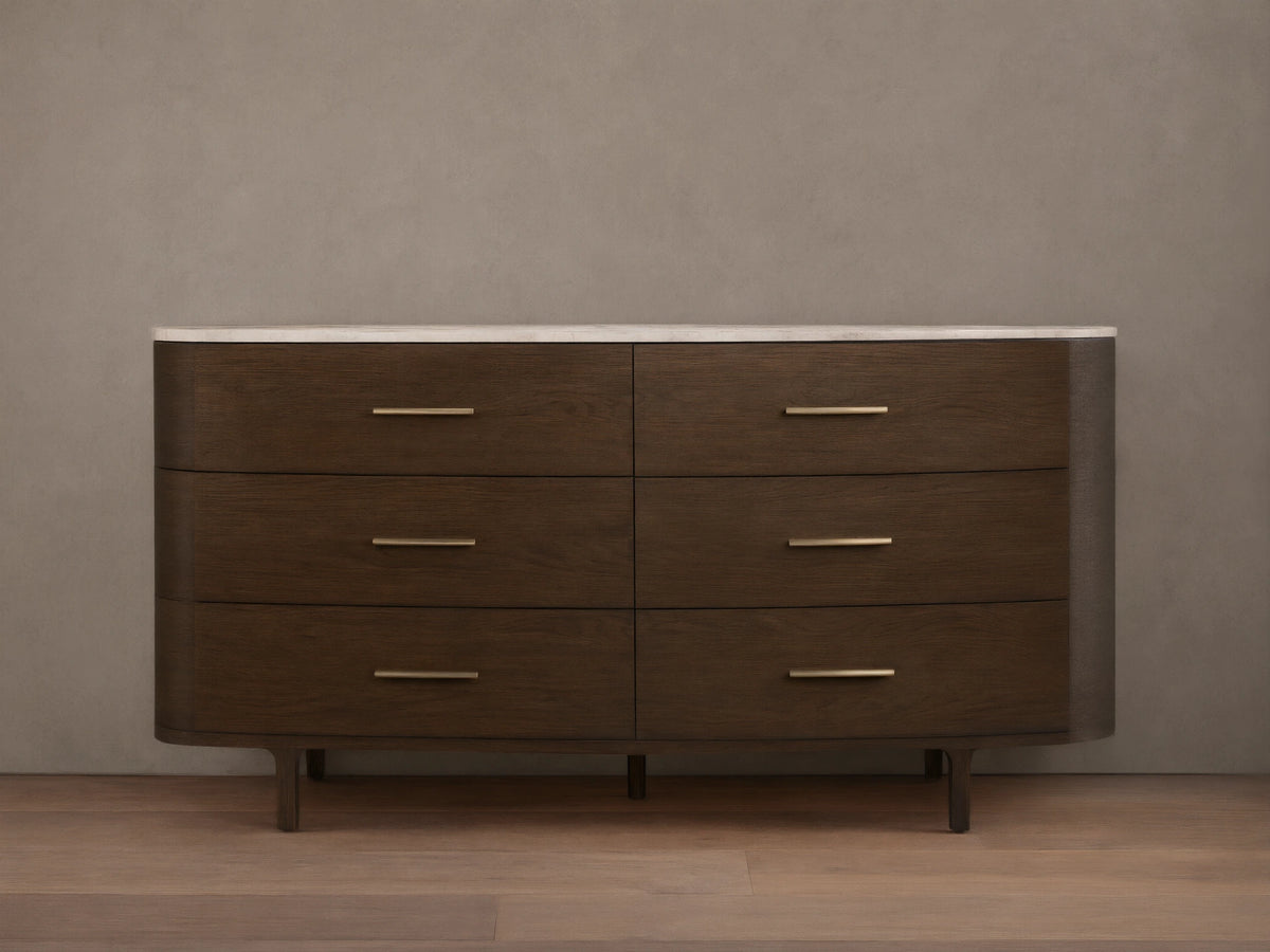 Danny Six-Drawer Dresser, dark oak with curved edges, white marble top, six drawers, brass pulls, on wooden floor.