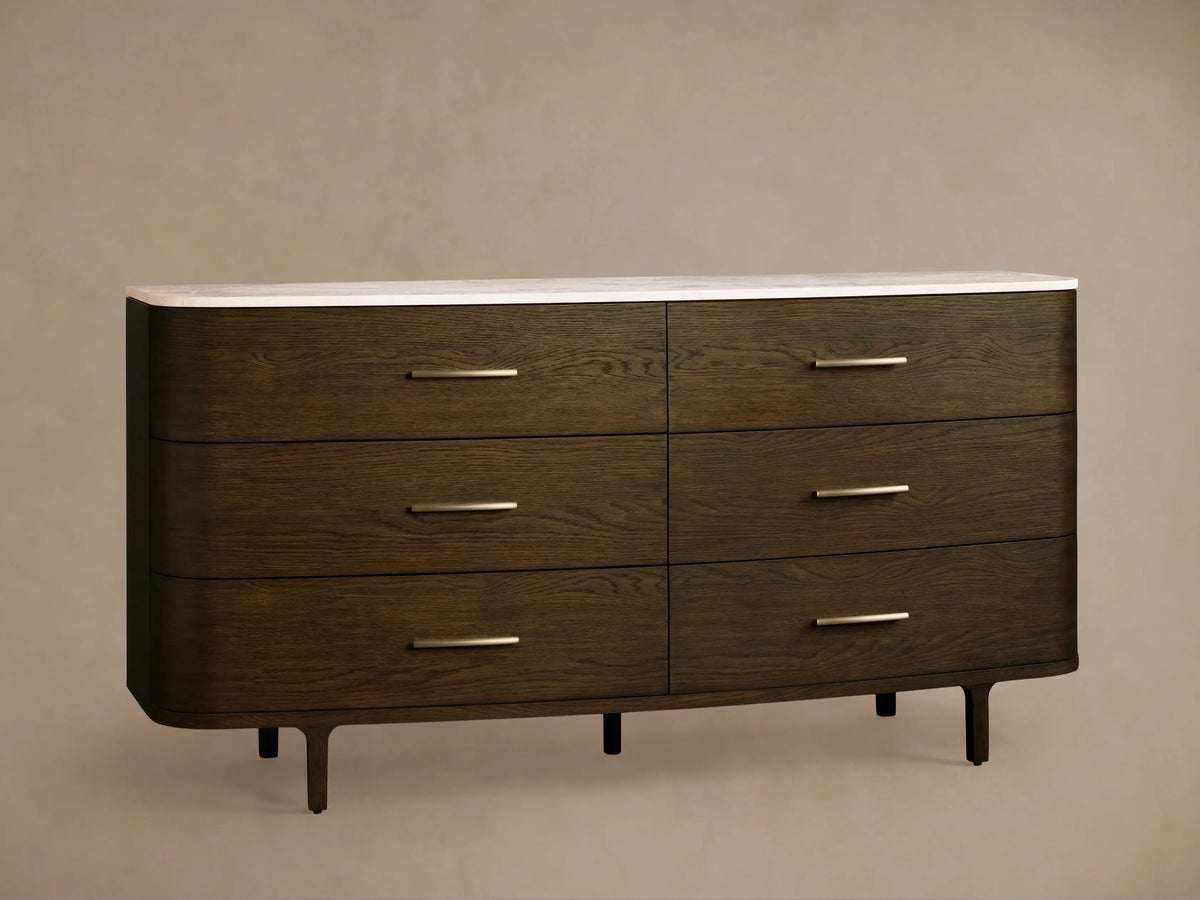 Danny Six-Drawer Dresser, dark oak with curved edges, white marble top, six drawers, brass pulls, on wooden floor.