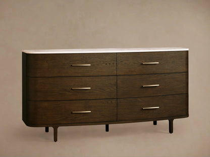 Danny Six-Drawer Dresser, dark oak with curved edges, white marble top, six drawers, brass pulls, on wooden floor.