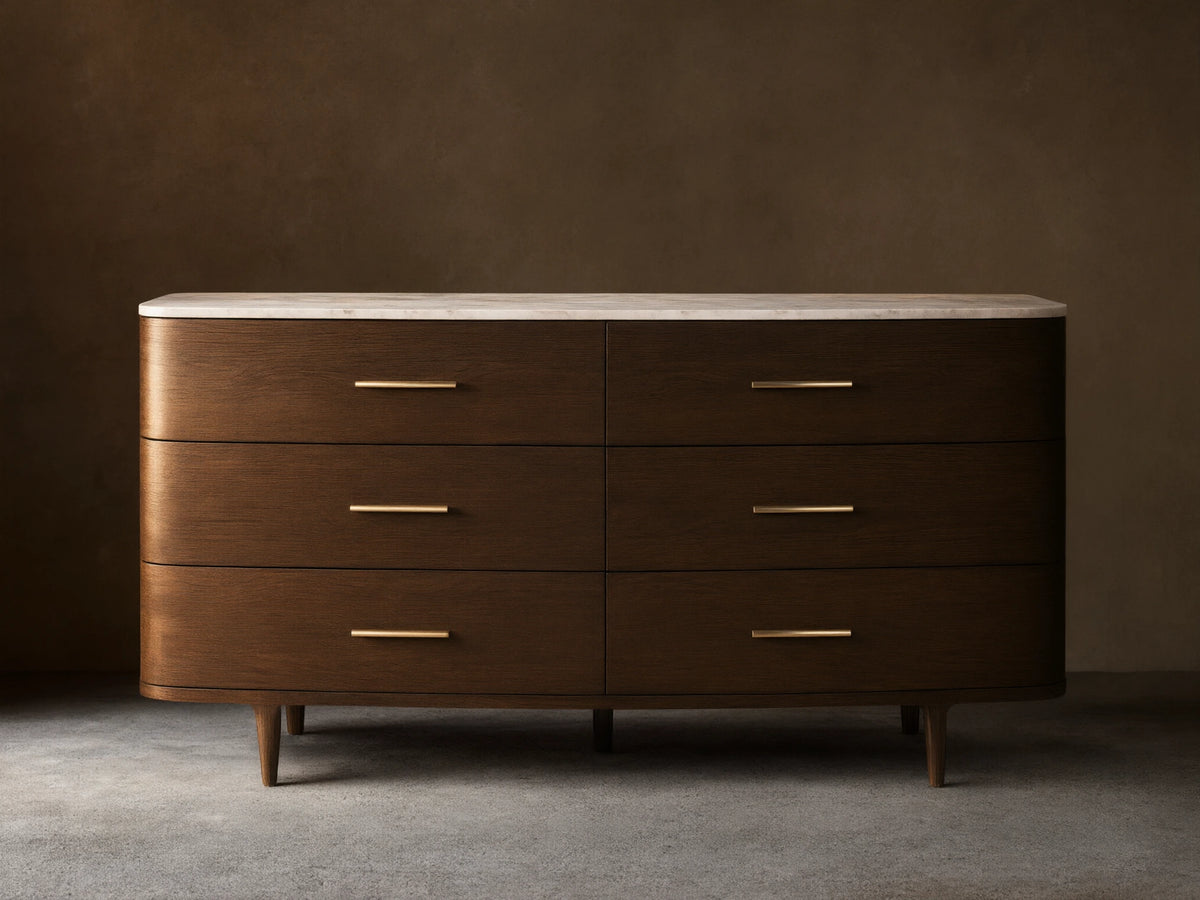 Danny Six-Drawer Dresser, dark oak with curved edges, white marble top, six drawers, brass pulls, on wooden floor.