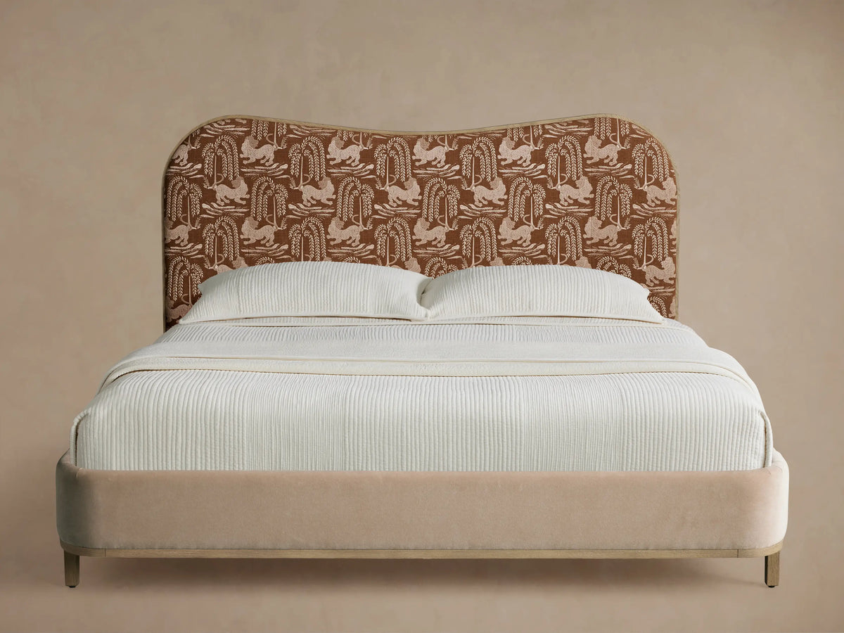 Danny Camelback Bed with an arched brown patterned headboard featuring animals & trees, beige upholstered frame, and white bedding.