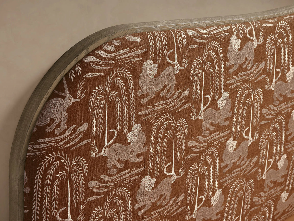Danny Camelback Bed with a camelback headboard in brown/beige lion and tree print, light beige upholstered frame, white bedding.