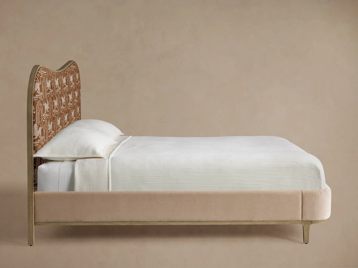 Close-up of Danny Camelback Bed's curved camelback headboard with grey wood frame, rust fabric, & silver lion & willow pattern.