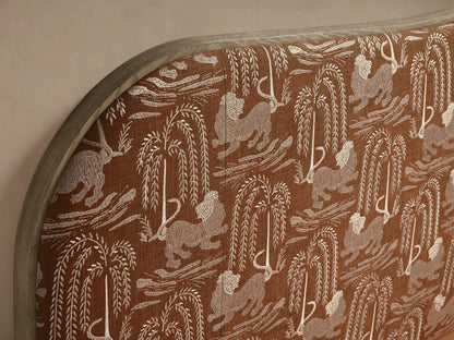 Danny Bed with camelback headboard featuring brown lion & willow pattern, light wood trim. White quilted bedding on a beige upholstered frame.