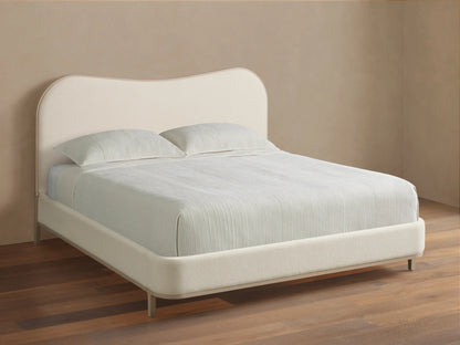 Danny Camelback Bed with a light beige upholstered camelback headboard & low frame, light grey legs. Striped bedding.