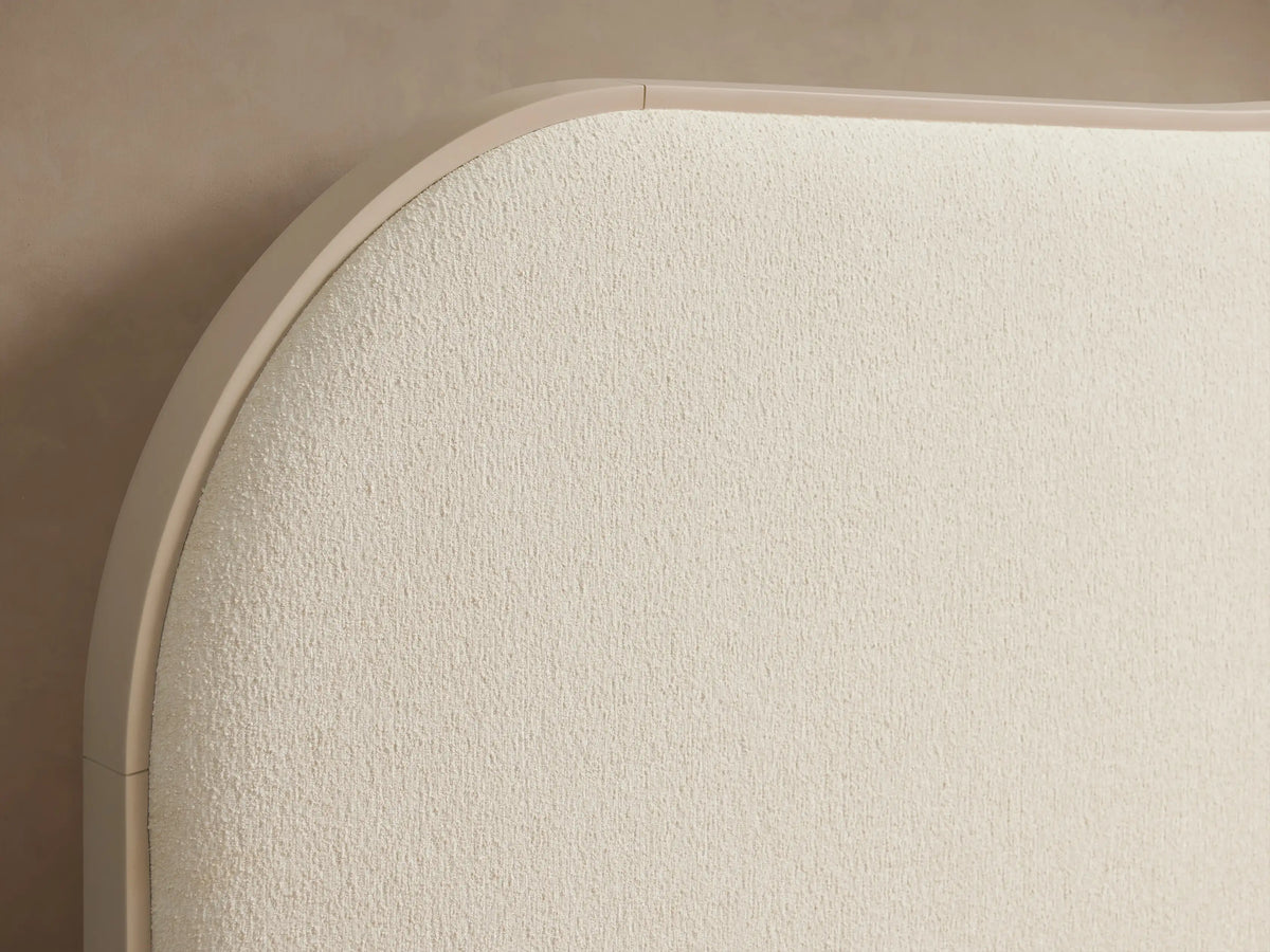 Danny Camelback Bed in light cream 'Fumo' fabric, with a camelback headboard, upholstered frame, and light ribbed bedding.