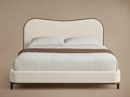 Front view of the Danny Camelback Bed. It has a brown patterned camelback headboard, a light brown upholstered base, and cream bedding.