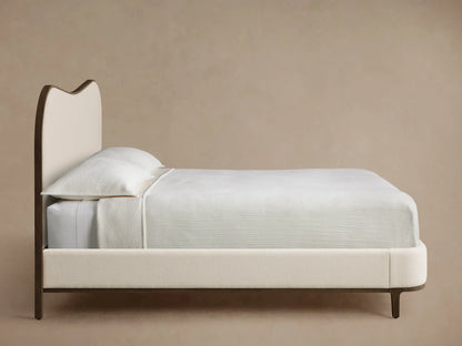 Danny Camelback Bed's curved headboard with dark oak trim framing creamy textured fabric upholstery.