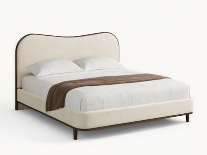 Cream upholstered Danny Camelback Bed with dark wood trim, light striped bedding, and a brown throw blanket.
