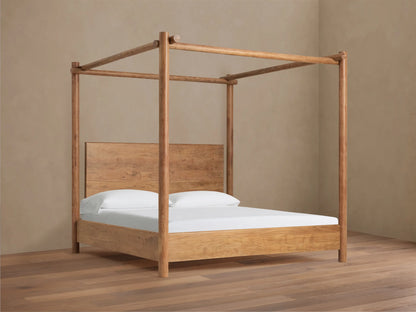 Dutton Canopy Bed, light brown acacia wood frame with matching headboard, white bedding. Set in a room with beige wall, wood floor.