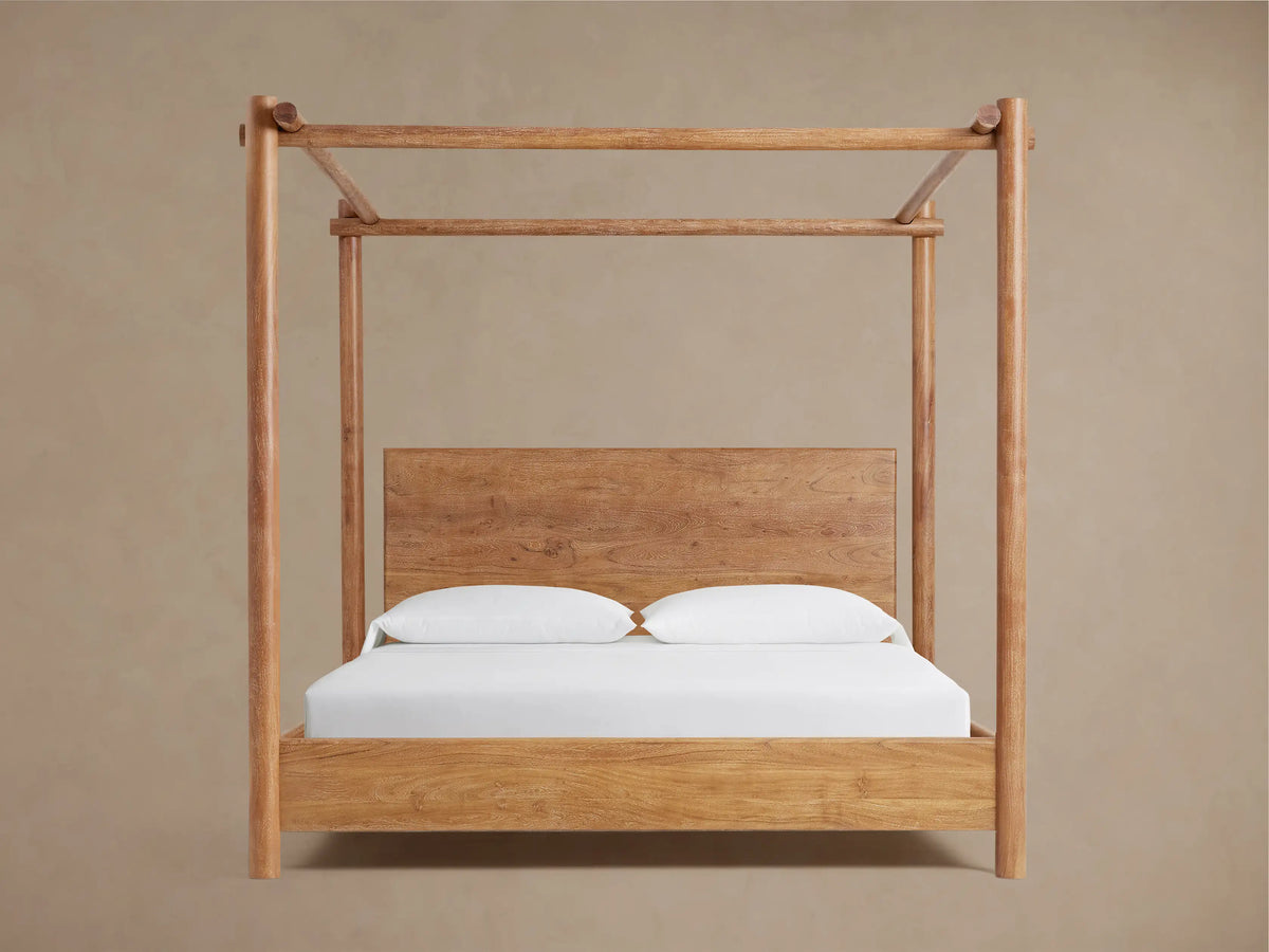 Dutton Canopy Bed, light brown acacia wood frame with matching headboard, white bedding. Set in a room with beige wall, wood floor.